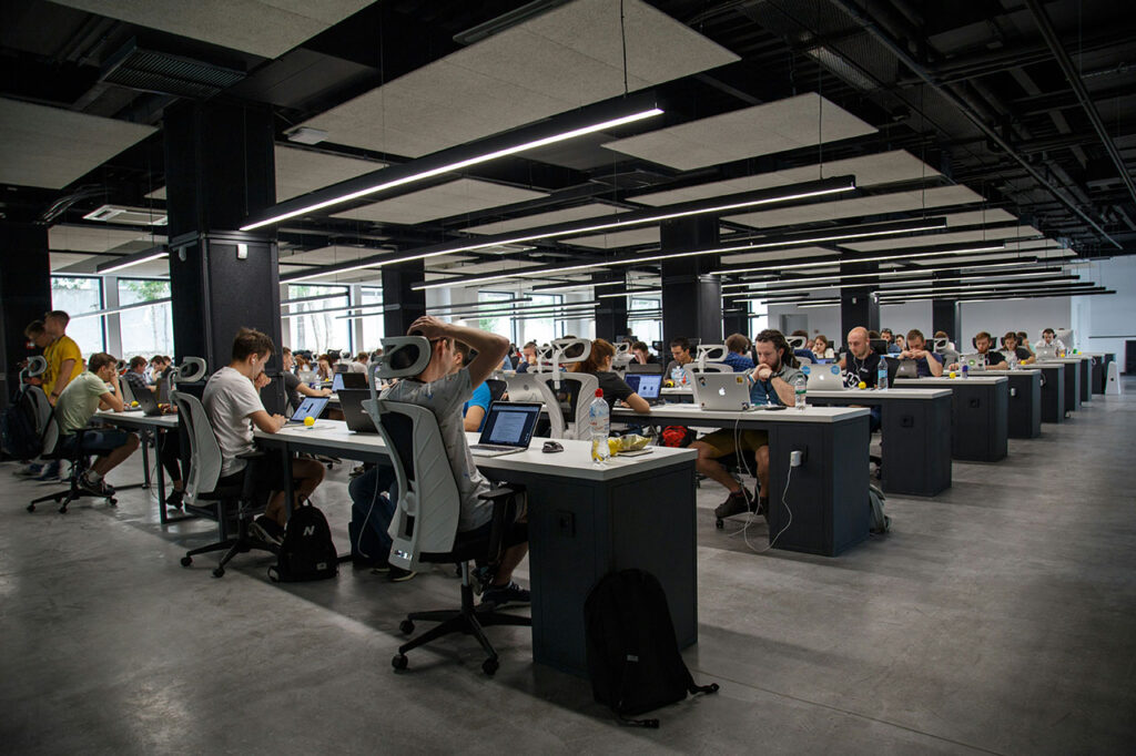 Modern open office workspace with employees collaborating at desks with laptops and computers